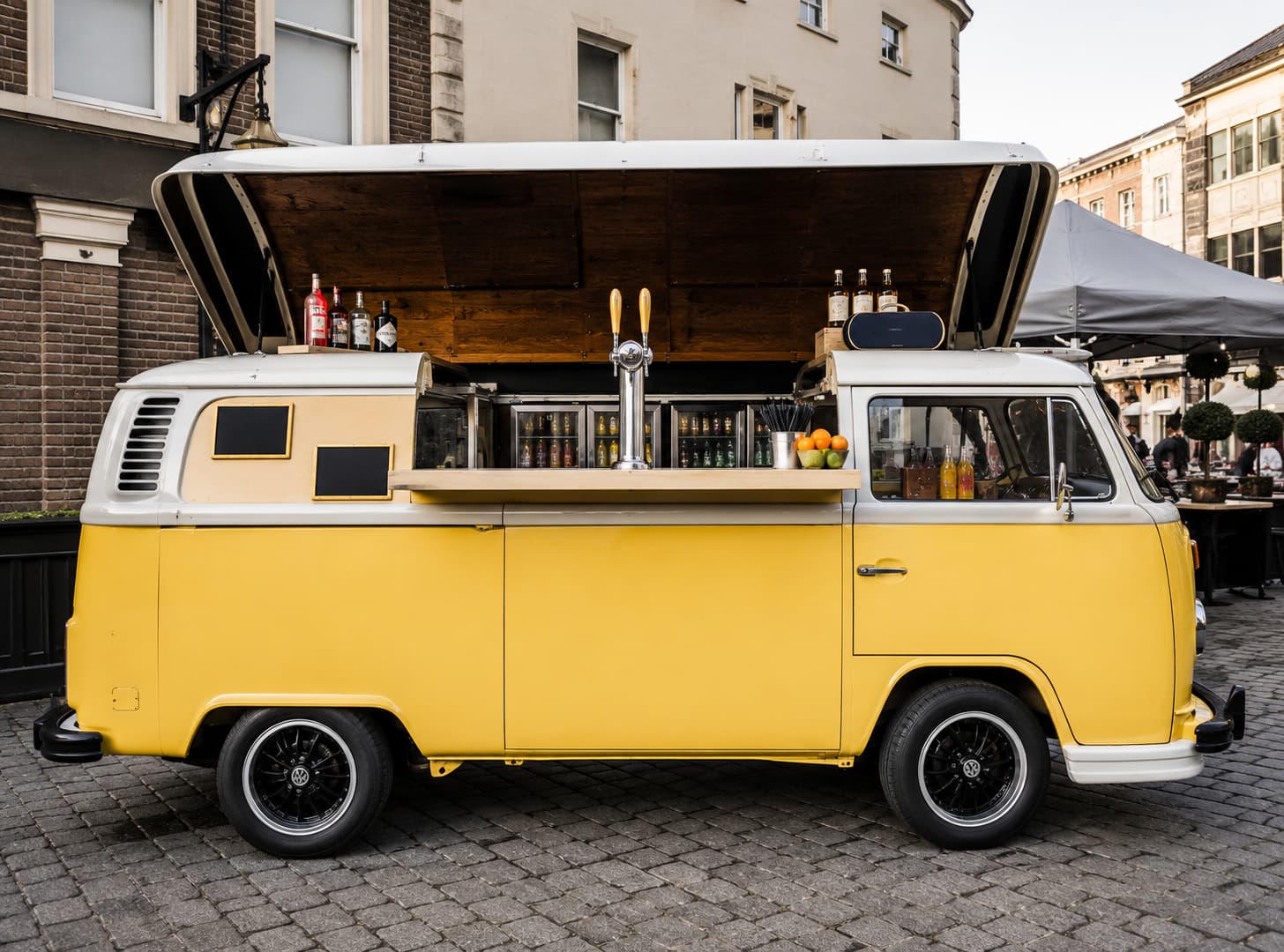 Yellow VW T2 full bar setup with beer tap and refrigerated display in cobblestone city square